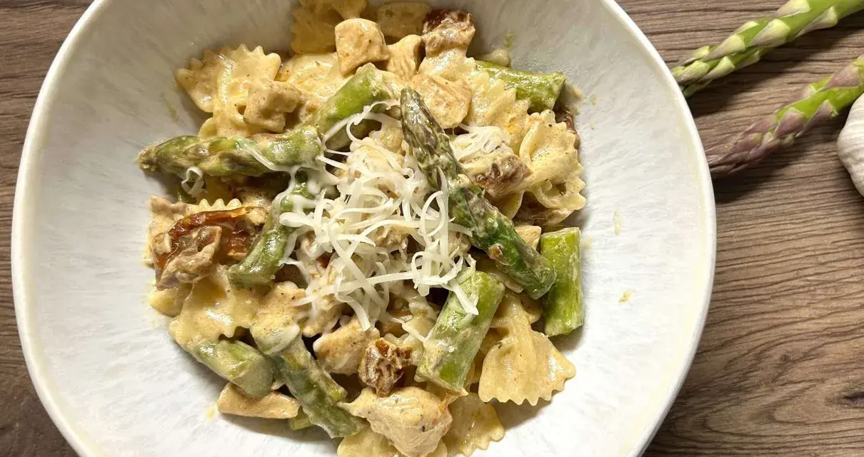 Pyszne makaron farfalle ze szparagami i kurczakiem w kremowym sosie, posypany startym parmezanem.