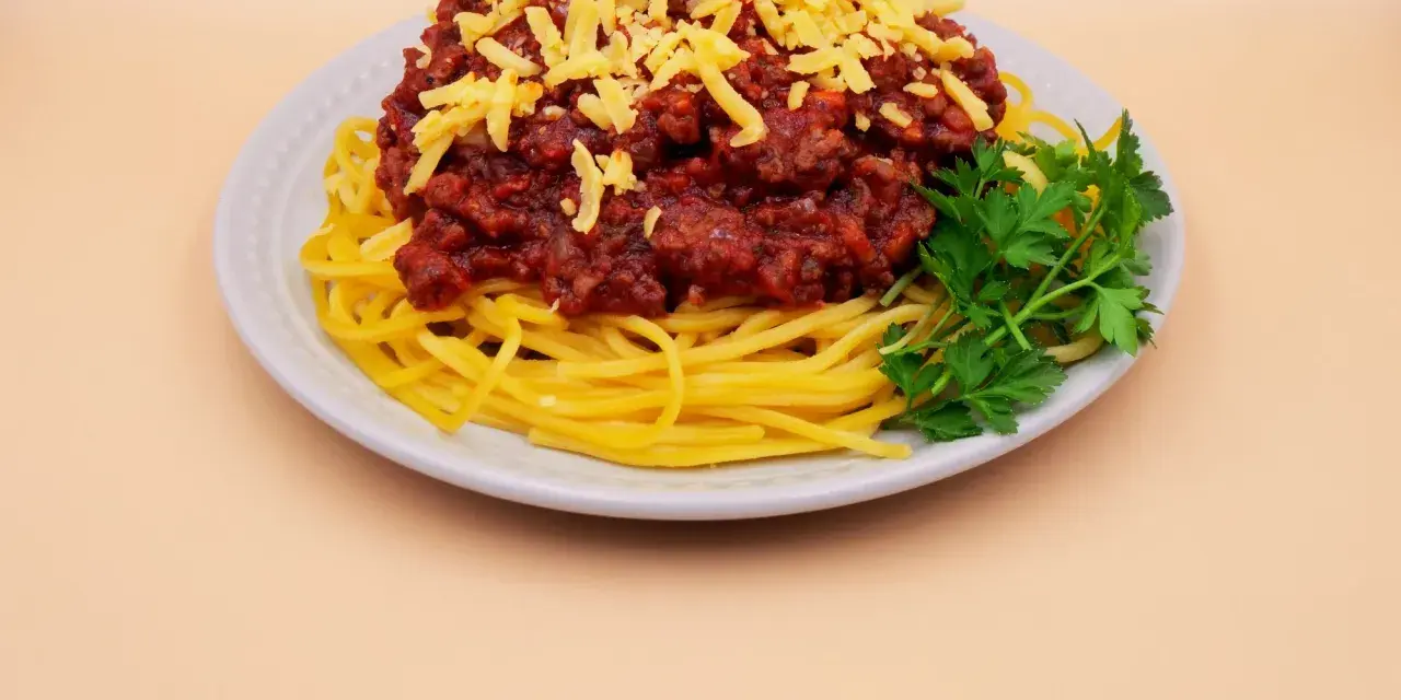 Prosty przepis na spaghetti z mięsem mielonym: makaron, sos boloński, starty ser i natka pietruszki na talerzu.