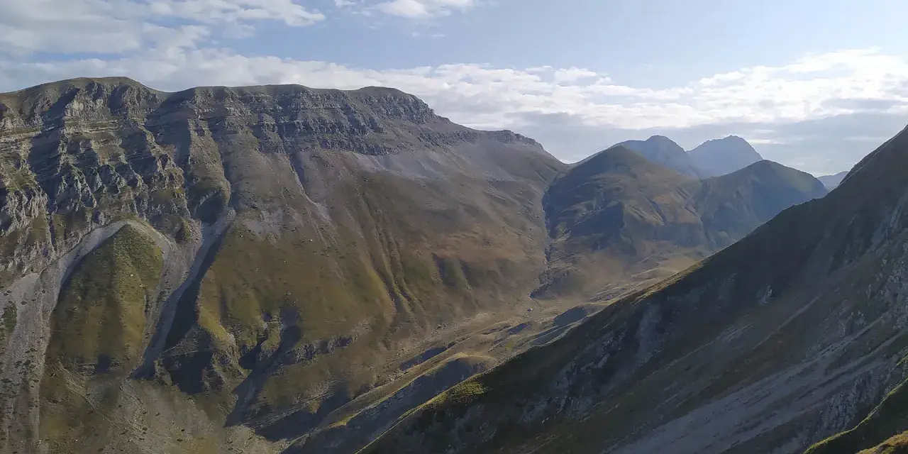 Vaste montagne del Monte Corvo sotto un cielo azzurro con nuvole bianche.