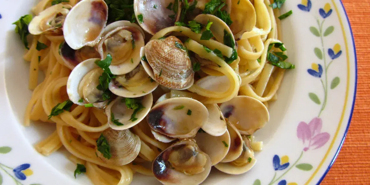 Pyszne spaghetti vongole z małżami i natką pietruszki na talerzu z kwiatowym wzorem.