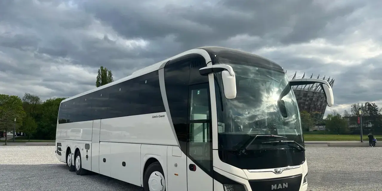 Biały MAN Lion's Coach, nowoczesny autokar turystyczny, zaparkowany na żwirowym placu pod pochmurnym niebem.