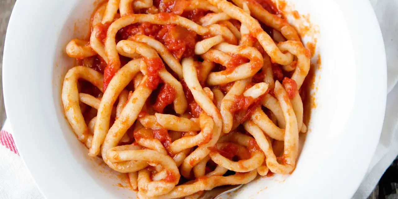 Piatto di pici fatti in casa conditi con un sugo rosso.