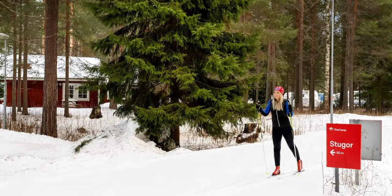 Kvinna på längdskidor vid Moraparken Camping. Röda stugor och granar i bakgrunden.
