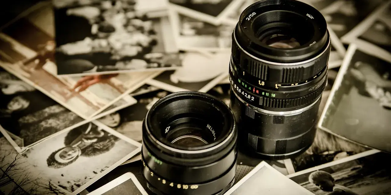 Dwa obiektywy aparatów leżą na starych, czarno-białych fotografiach.