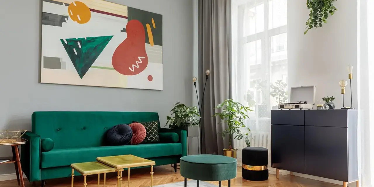 Soggiorno moderno con divano verde smeraldo e tavolini dorati. L'arte astratta sul muro grigio e i mobili scuri creano un perfetto abbinamento colori pareti e mobili.