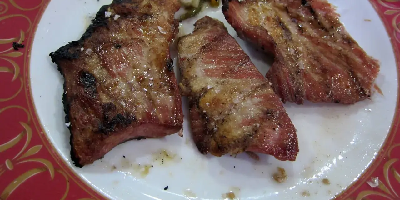 Tres trozos de secreto de cerdo a la parrilla, jugosos y con sal gruesa, servidos en un plato blanco con borde rojo.