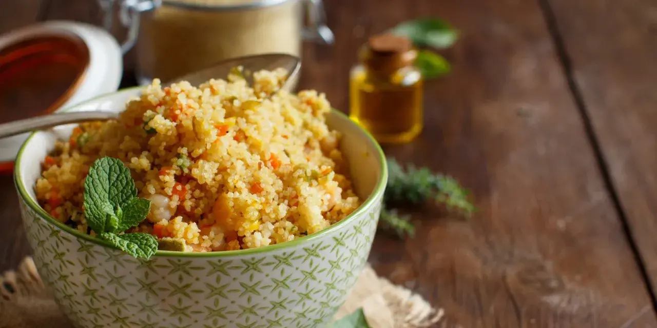 Schüssel mit buntem Couscous, garniert mit Minze. Daneben ein Glas Couscous und eine kleine Flasche Öl. Ein köstlicher Couscous-Baby-Genuss!