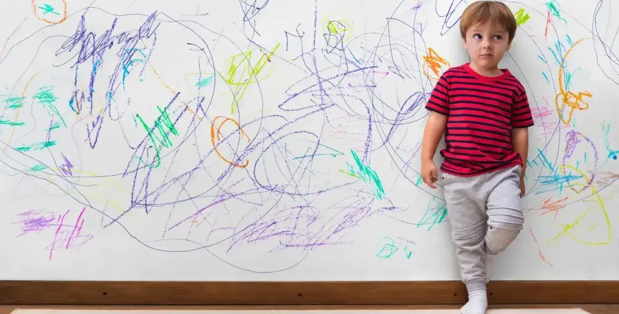 Chłopiec z ADHD, stojący przy ścianie pokrytej kolorowymi bazgrołami, wyraża swoje emocje.