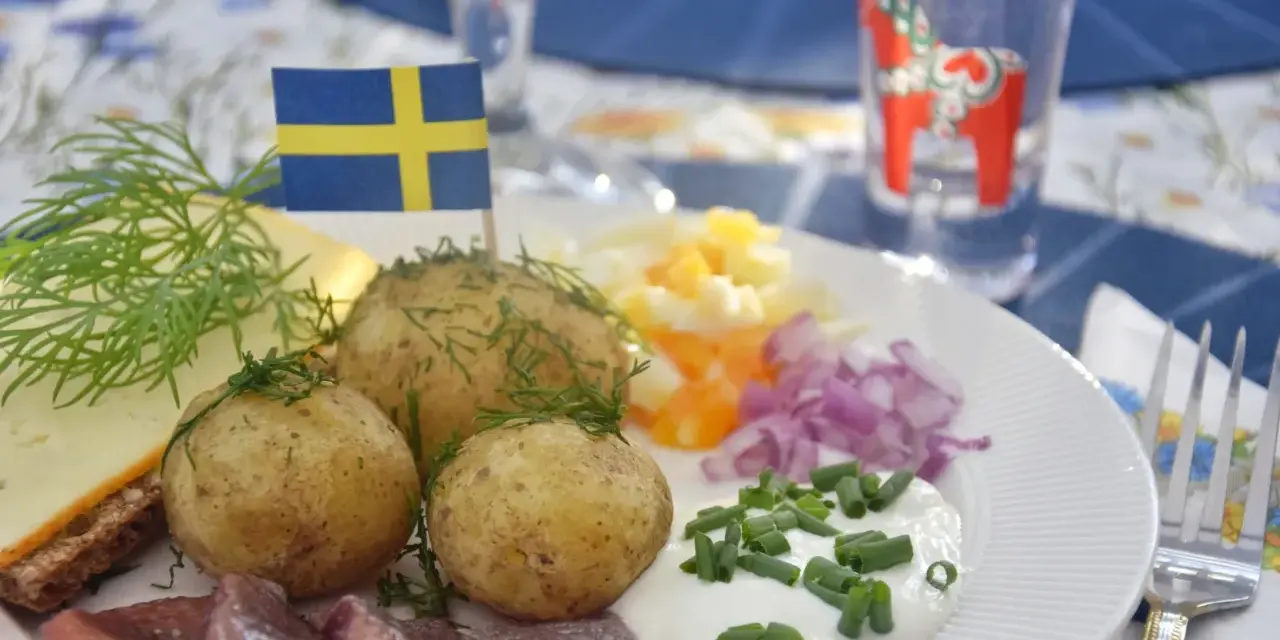 En tallrik med sill, färskpotatis, ost och dill. En svensk flagga vajar stolt. Perfekt mat midsommar!
