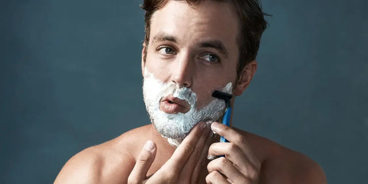 Hombre con espuma de afeitar en la cara, aprendiendo como afeitarse la barba con una maquinilla.