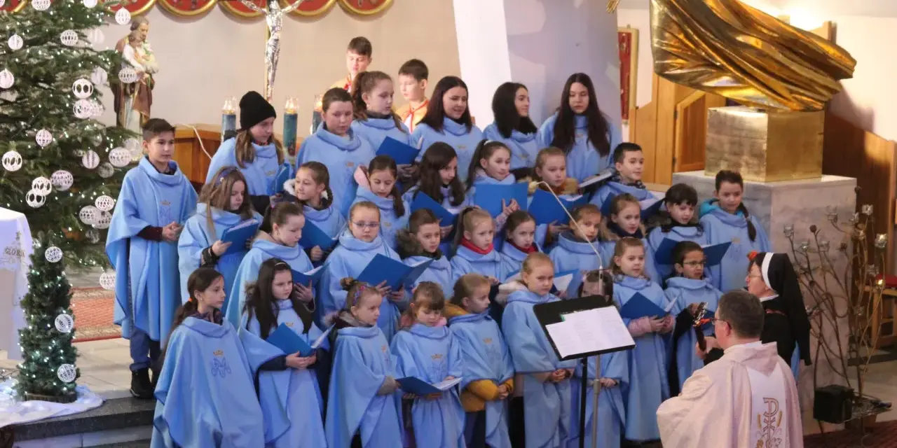 Dzieci w błękitnych strojach tworzą schola, śpiewając w kościele przy choince.