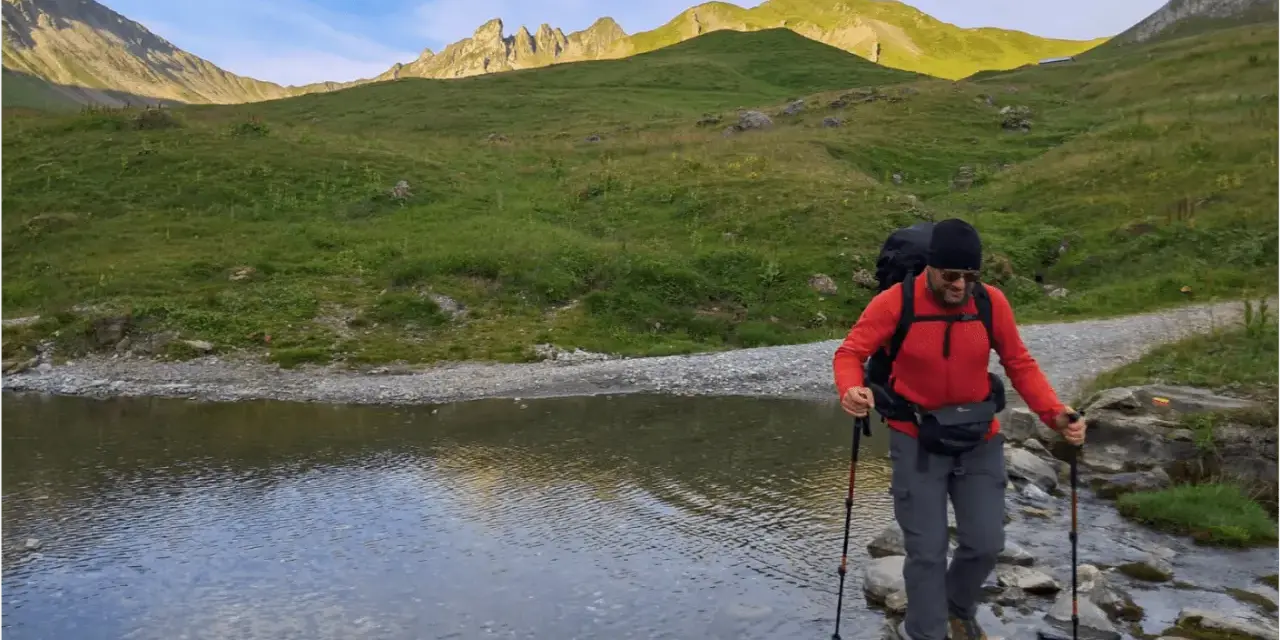 Un randonneur traverse un ruisseau de montagne, bâtons en main. Une belle illustration de pourquoi marcher avec des bâtons pour plus de stabilité.