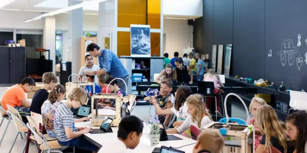 Children engage in 3d printing education, working with laptops and 3D printers in a bright, modern classroom.