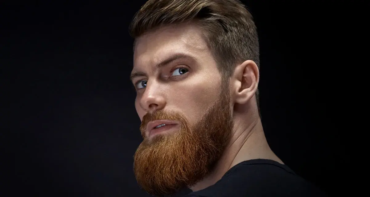 Hombre con barba rojiza y peinado actual, con el pelo peinado hacia atrás y un corte moderno.