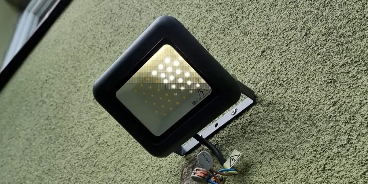 Czarna lampa led żarzy się po włączeniu, oświetlając zieloną, chropowatą ścianę. Widać przewody i złączki.
