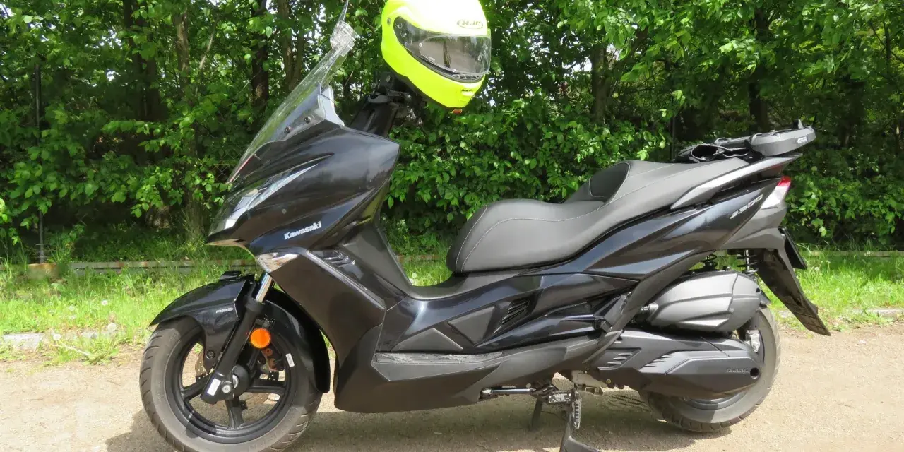 Czarny skuter Kawasaki J300 z jaskrawożółtym kaskiem zawieszonym na kierownicy, gotowy do jazdy w słoneczny dzień.