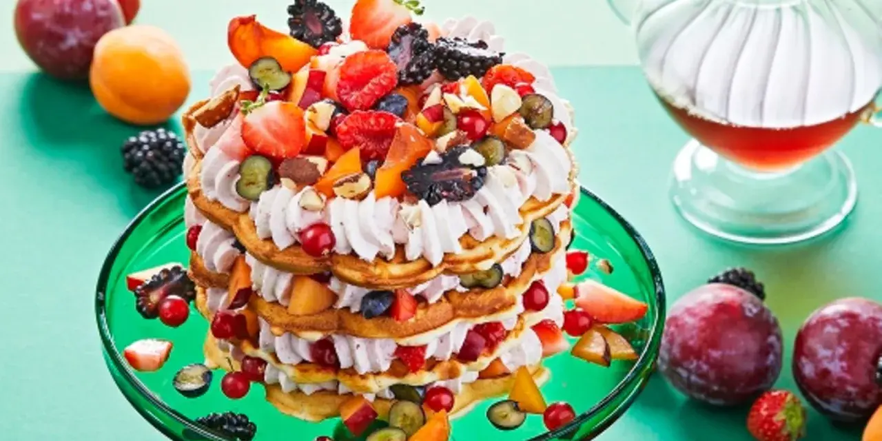 Eine beeindruckende Waffeltorte mit Erdbeeren und Mascarpone, geschichtet mit frischen Beeren und Früchten, auf einem grünen Teller.