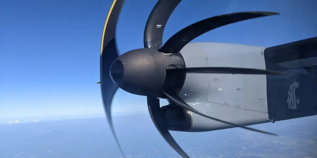 Wirujący śmigłowiec samolotu z efektem rolling shutter nad miastem i górami w oddali.