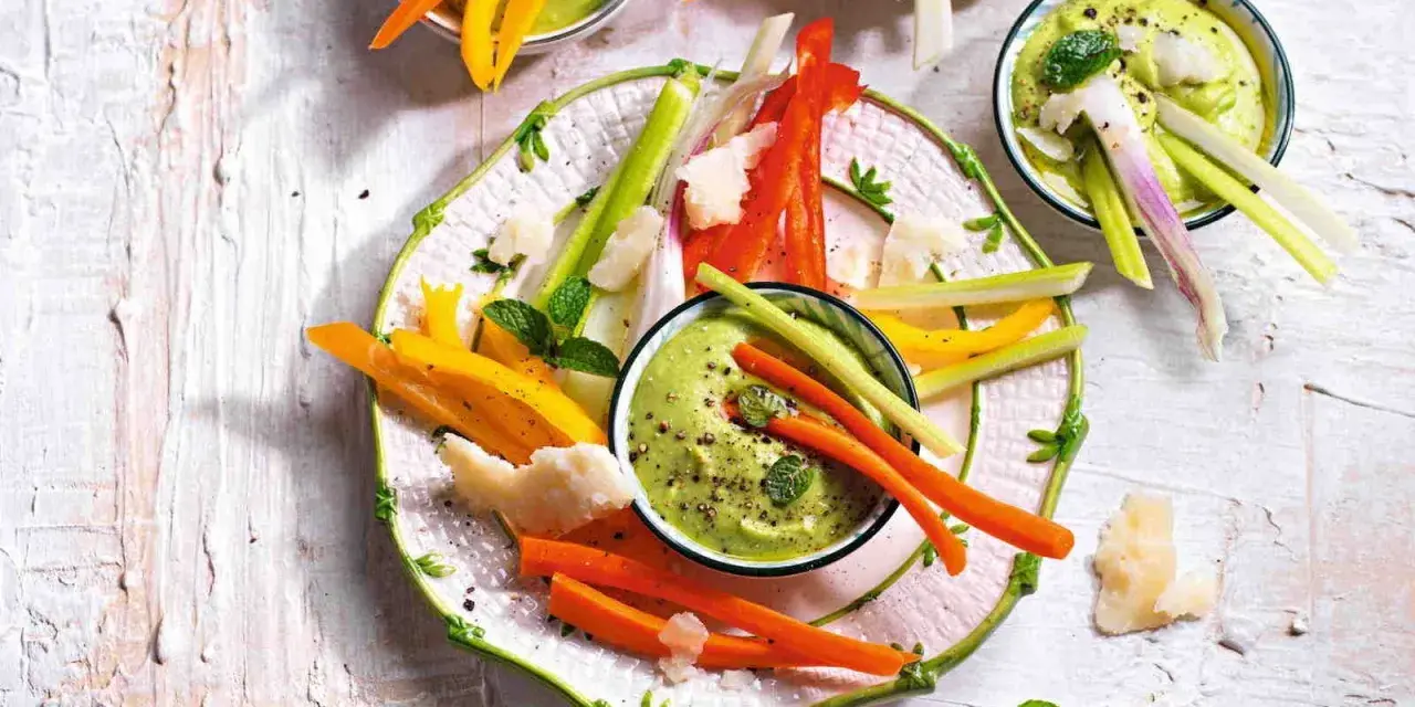 Deliziosi antipasti vegetariani: bastoncini di carote, peperoni e sedano con salsa verde cremosa, guarniti con scaglie di formaggio e menta.