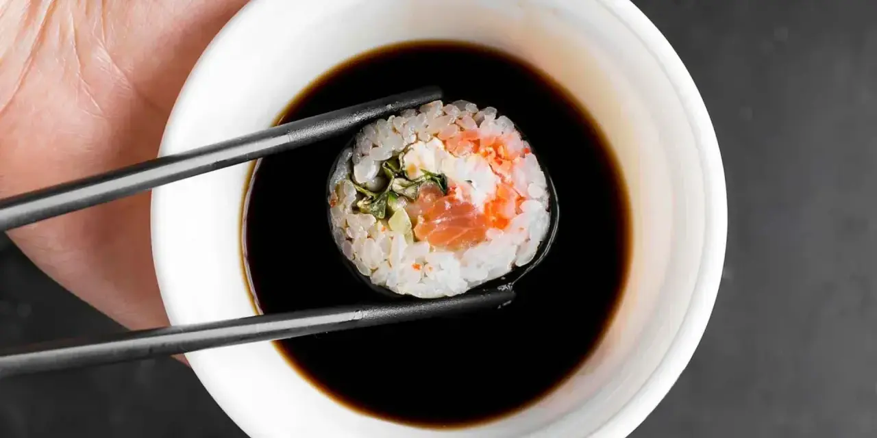 Pałeczkami zanurzam sushi w sosie do sajgonek. Widać kawałek łososia i ryż.