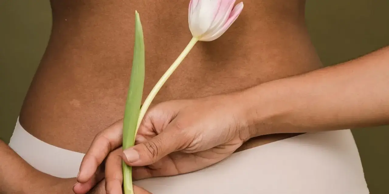 Delikatne rozstępy na plecach, ukryte za tulipanem. Ciało w beżowej bieliźnie.