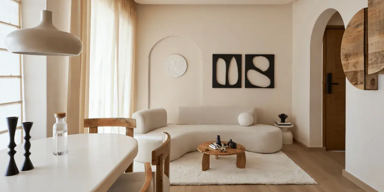 Un soggiorno in stile wabi sabi con divano curvo, tavolino in legno grezzo, tappeto soffice e decorazioni minimaliste.