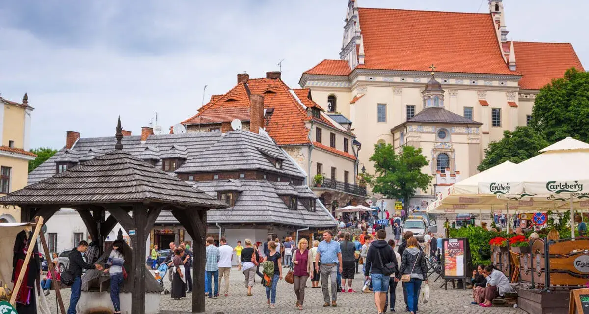 Tłum ludzi spaceruje po brukowanym rynku, podziwiając zabytkową architekturę. To urokliwe turystyczne miasta w Polsce.