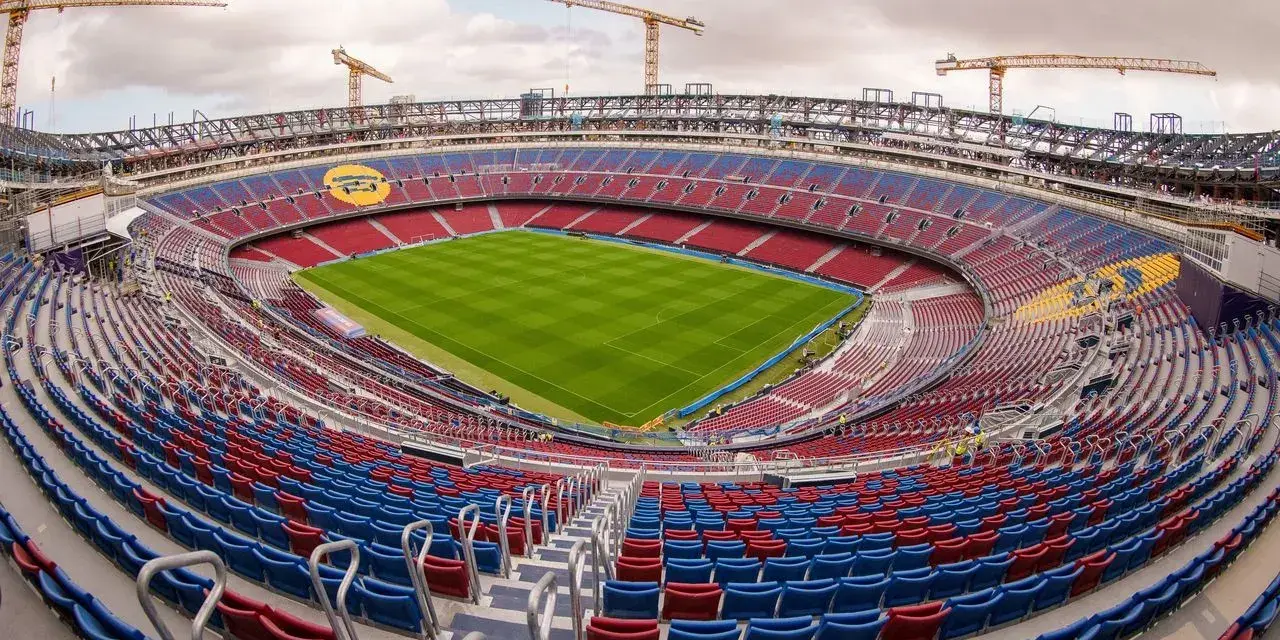 Stadion de la Cartuja w budowie, z widocznymi dźwigami i częściowo wykończonymi trybunami w kolorach czerwonym i niebieskim.