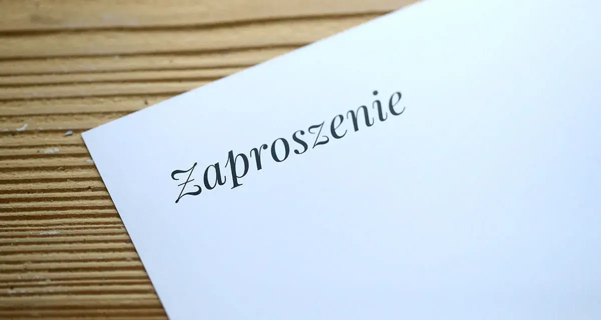 Eleganckie zaproszenie na ślub na białym, satynowym papierze, leżące na drewnianym tle.