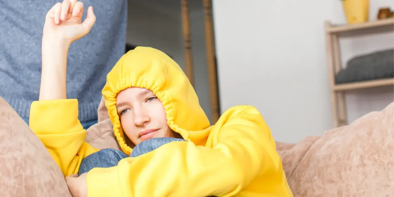 Ein Teenager in gelbem Hoodie zeigt seiner Mutter den Mittelfinger. Er hat keinen Respekt vor ihr.
