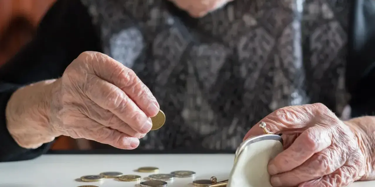 Dłoń starszej osoby liczy monety, zastanawiając się, kiedy najlepiej przejść na emeryturę w 2026 roku.