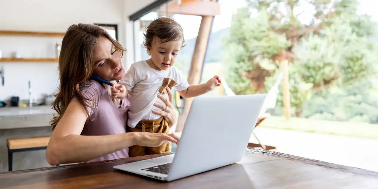Als alleinerziehende Mutter jongliert sie Arbeit und Kind. Sie telefoniert, während sie ihr Kleinkind hält und am Laptop tippt.