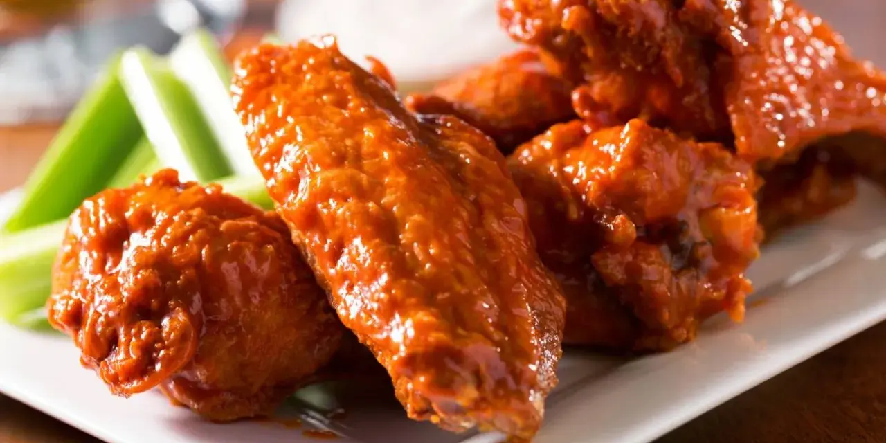 Alitas de pollo en freidora de aire, cubiertas de salsa picante, servidas con bastones de apio crujientes. ¡Un aperitivo irresistible!