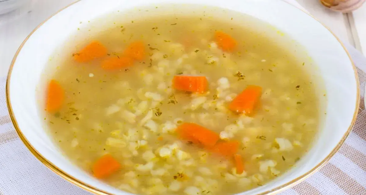 Aromaticzna zupa na rosole z makaronem i marchewką, podana w białej miseczce ze złotym rantem.