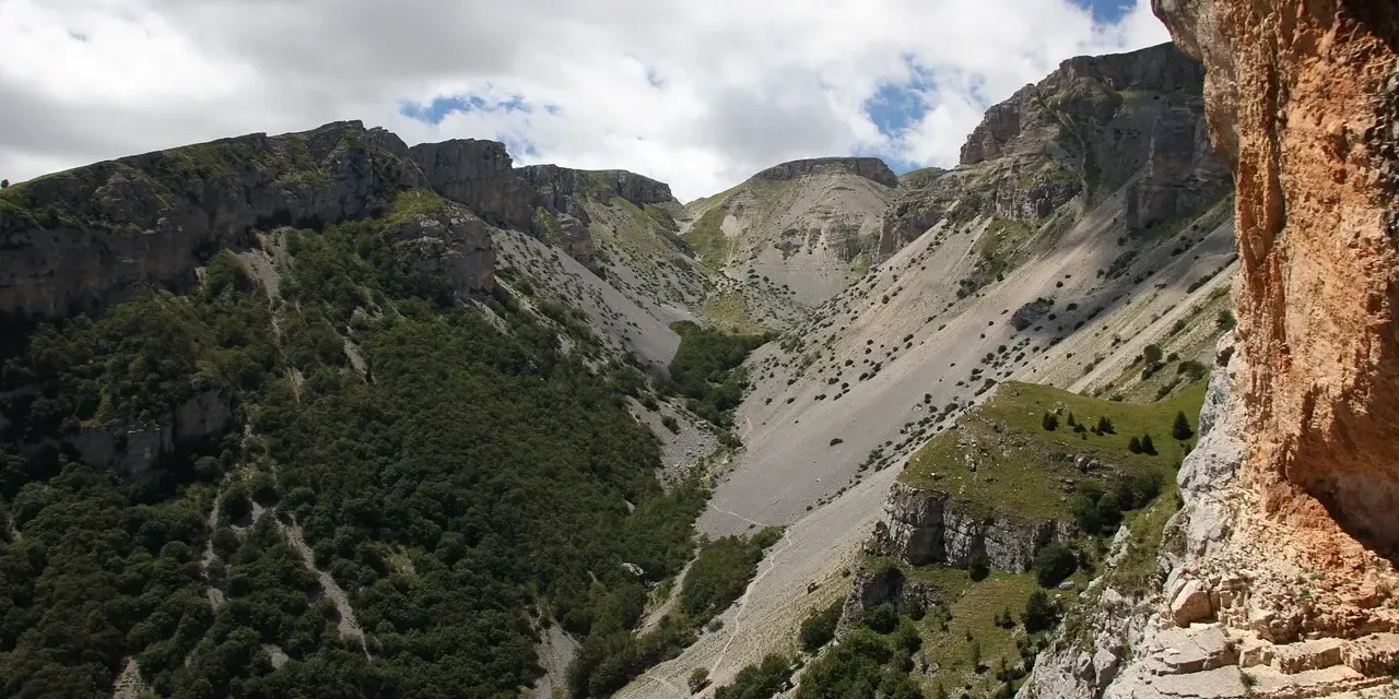 Un sentiero serpeggia tra montagne rocciose e vegetazione rigogliosa, un'avventura estiva al passo lanciano.