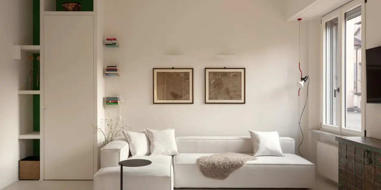 Soggiorno luminoso con divano bianco, quadri antichi e arredi funzionali, perfetto per case piccole ben arredate.
