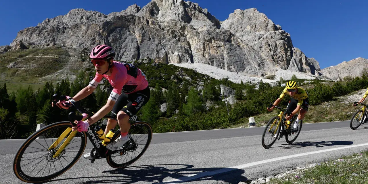 Cyclist in pink jersey, likely the winner of the Giro d'Italia, climbs a mountain road with a dramatic rocky peak behind.