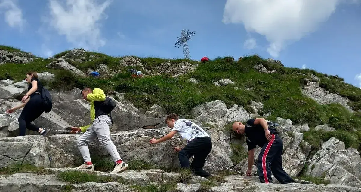 Grupa turystów wspina się po kamienistym zboczu, pokonując najtrudniejszy szlak na Giewont. W tle widoczny krzyż.