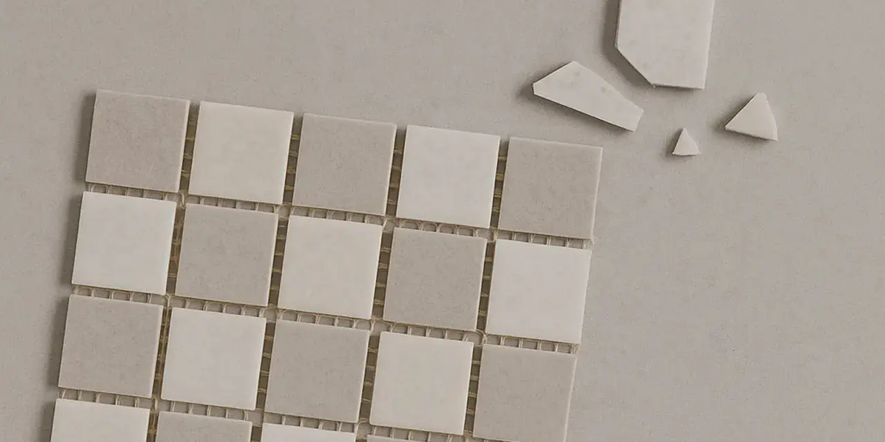 Små, ljusa mosaikplattor i grå och vita nyanser, några trasiga bitar ligger bredvid. Perfekt för att torka papper eller skapa ett mönster.