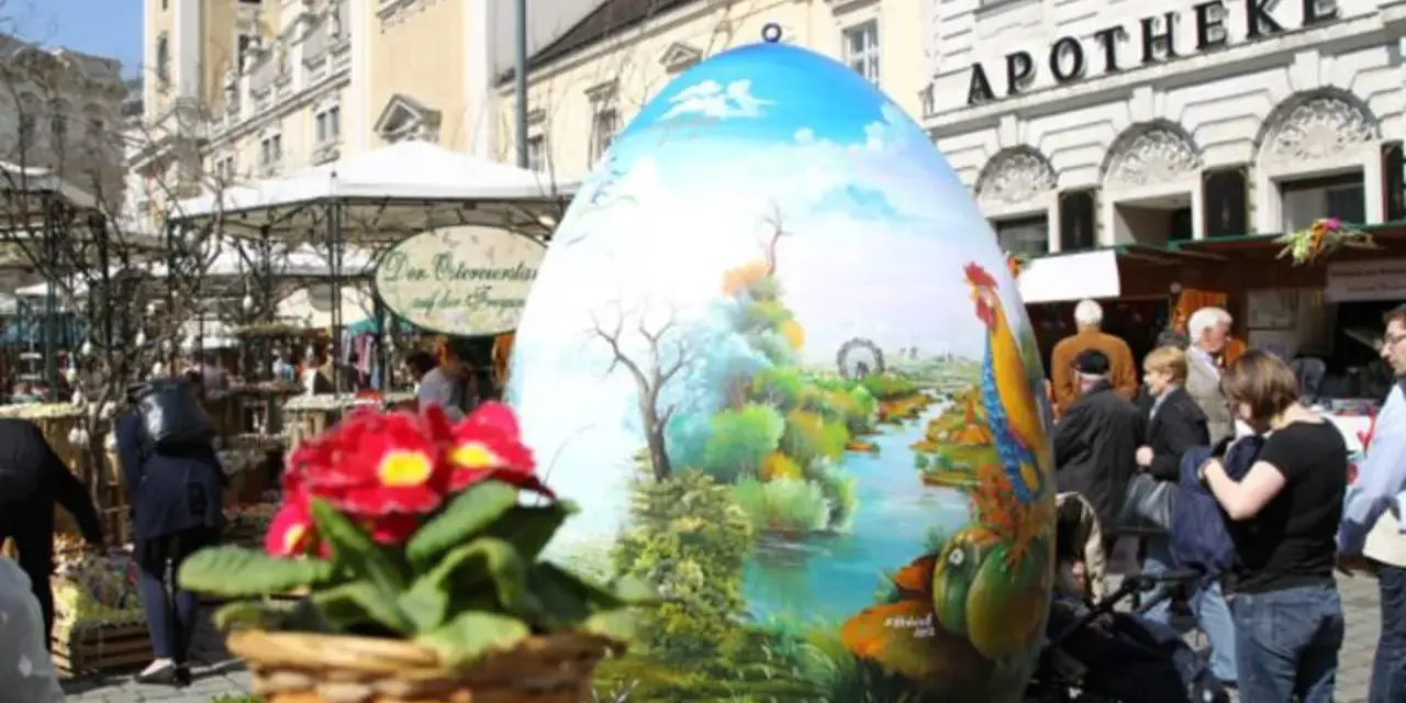 Großes, bemaltes Ei mit Frühlingslandschaft und Hahn, ein Osterbrunnen, der erklärt, warum ist Ostern immer wann anders.