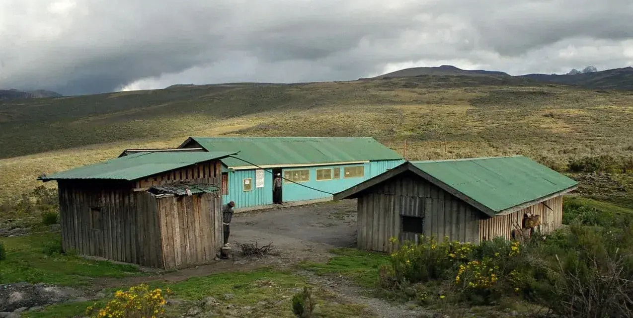 Proste chatki z zielonymi dachami na tle surowego krajobrazu u podnóża góry Mt Kenya.