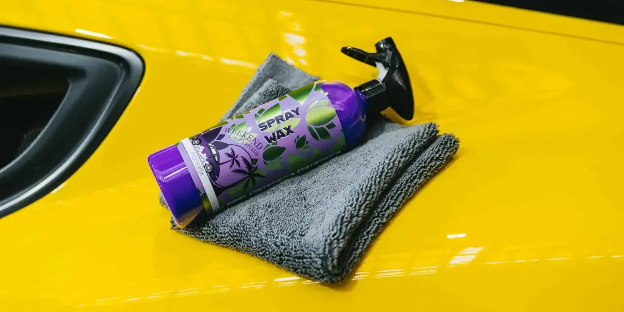En flaska spray wax ligger på en gul bil med en grå mikrofiberduk.