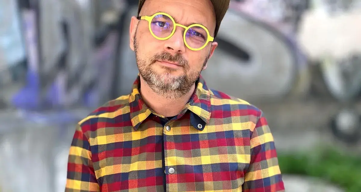Filip Springer w okularach i koszuli w kratę, na tle graffiti.