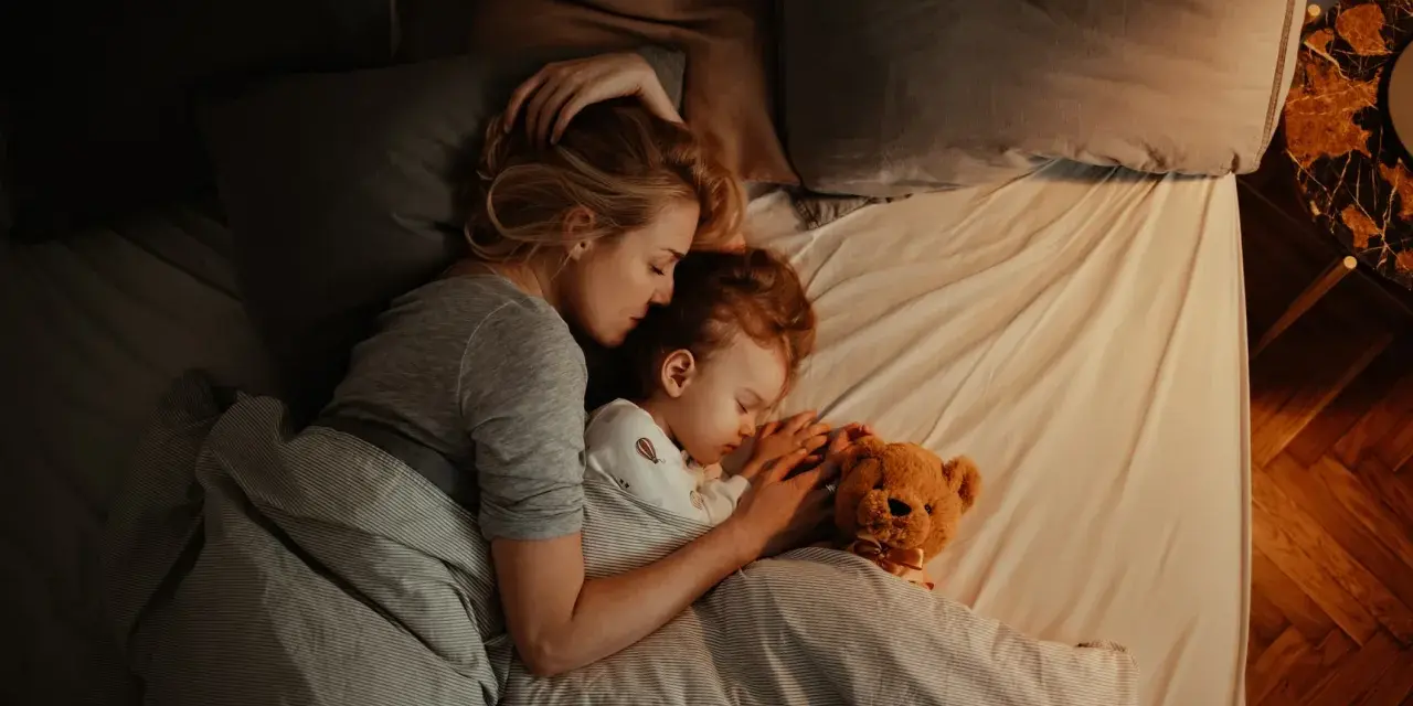 Mutter und Kind schlafen eng umschlungen. Ab wann Babys bewusst kuscheln, zeigt diese Szene der Geborgenheit.