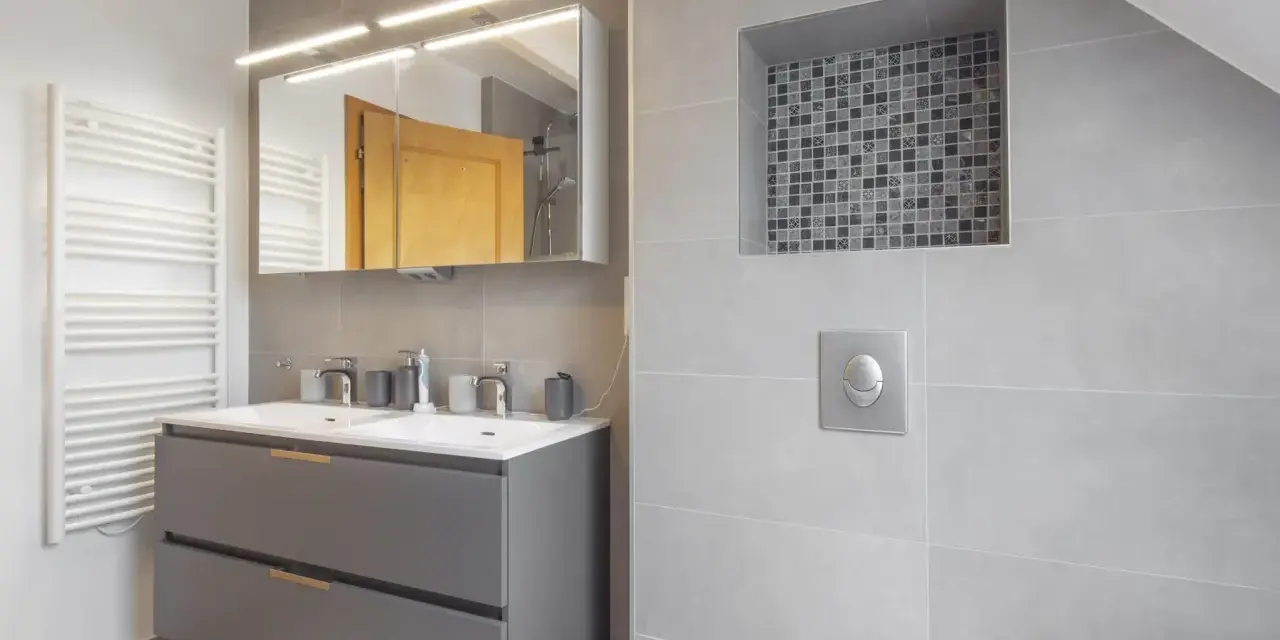 Salle de bain moderne avec double vasque, radiateur blanc et un choix carrelage gris subtil, agrémenté d'une niche décorative en mosaïque.