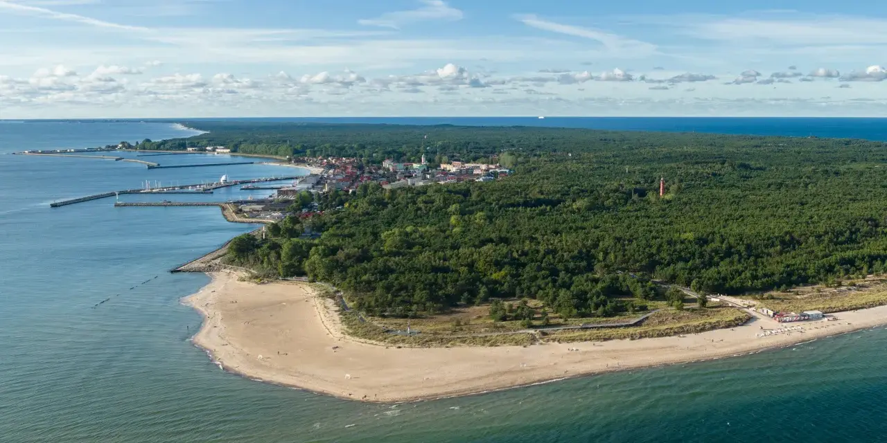 Widok na zatokę pucką z lotu ptaka. Widać piaszczystą plażę, las sosnowy, miasteczko z portem i latarnię morską.