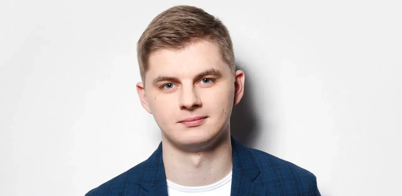 Młody mężczyzna w niebieskiej marynarce w kratę, gotowy do występu. Polski stand up w jego wykonaniu to gwarancja dobrej zabawy.