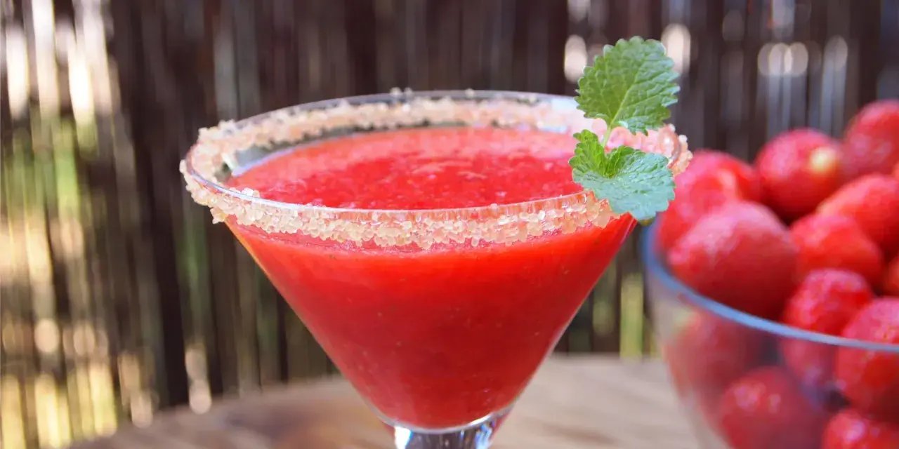Orzeźwiający strawberry daiquiri z cukrowym rantem i listkiem mięty, obok miska pełna świeżych truskawek.