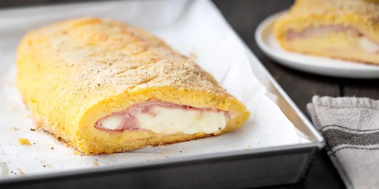 Rotolo dorato di polpettone di patate ripieno di prosciutto e formaggio filante, pronto per essere gustato.