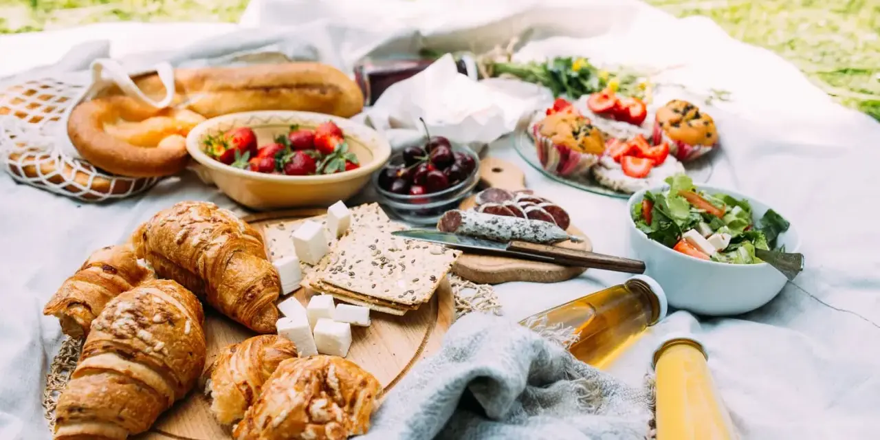 Pyszne jedzenie na piknik: świeże pieczywo, owoce, sałatka, sery i napoje.